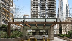 Ein Außenbereich mit einer Holzpergola, Sitzgelegenheiten und einer Steinstruktur, die als Küche oder Bar dienen könnte.