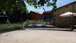 An outdoor patio area with tables and chairs, a stone building, and a fenced garden. - Cozy roulotte, pets welcome - 4 guests (Saint-Paulien)