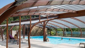 Et udendørs swimmingpool med et overdækket område, klare himmel og en person, der svømmer.