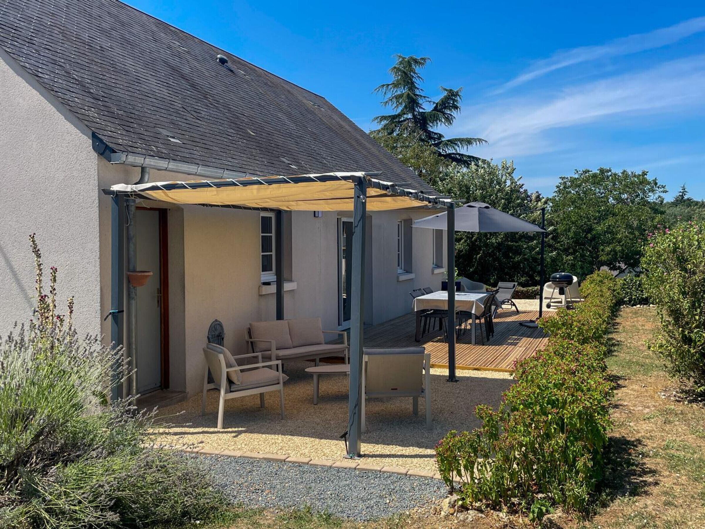 Un espace extérieur aménagé avec une zone de repos couverte, comprenant une table et des chaises, un barbecue et une pergola offrant de l’ombre.