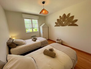 Een slaapkamer met twee bedden, een raam, een bladdecoratie aan de muur, een hanglamp en een kleine mand.