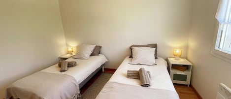 Un dormitorio con dos camas individuales, mesitas de noche con lámparas, una lámpara colgante de techo tejida y una ventana con cortinas.