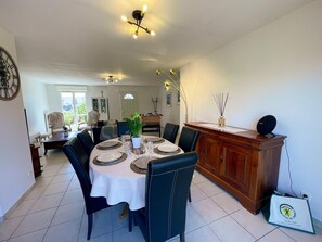 A dining area with a round table set for six, surrounded by chairs. There is a wooden cabinet with a speaker on top, and a clock on the wall. - Single-story house in Chenonceaux - 6 guests (Chenonceaux)