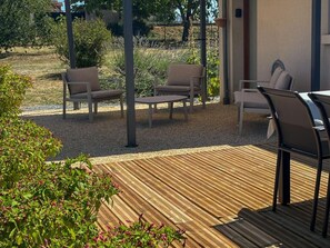 An outdoor patio area with a wooden deck, two beige chairs, a small table, and a partial view of a building. - Single-story house in Chenonceaux - 6 guests (Chenonceaux)