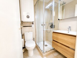 A modern bathroom with a toilet, a glass shower enclosure, and a wooden vanity with a sink. - Apartment canal view with parking - 4 guests (Sète)