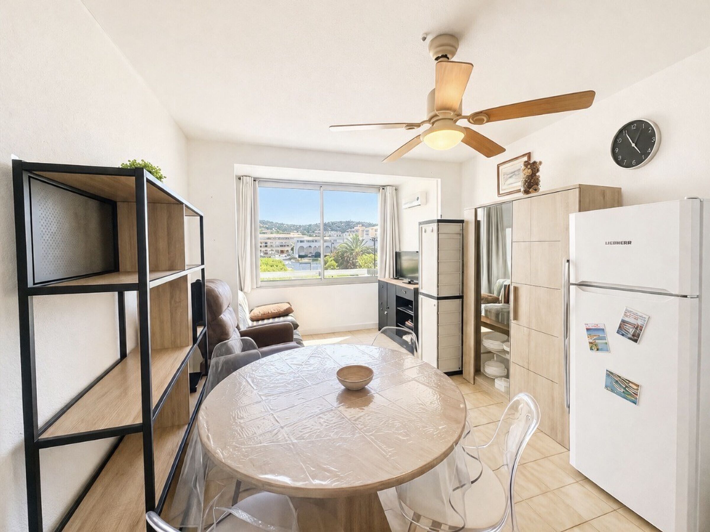 A compact kitchen with a dining table, chairs, a refrigerator, and a ceiling fan.