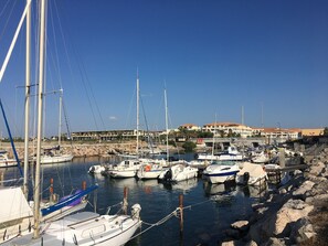 Ein Yachthafen mit verschiedenen Schiffen, einer felsigen Küstenlinie und einem Gebäude mit mehreren Balkonen im Hintergrund.