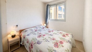 A bedroom with a bed, a nightstand, a lamp, a ceiling fan, and a window with curtains. - Apartment canal view with parking - 4 guests (Sète)