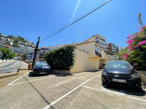 Ein Parkplatz mit zwei Autos, ein Gebäude mit Balkonen und einem strahlend blauen Himmel.