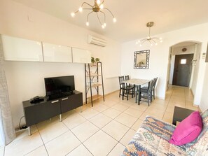 Ein modernes Wohnzimmer mit Fernseher, einer Couch, einem Esstisch und Stühlen.