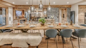 A dining area with a long wooden table set for a meal, surrounded by chairs, and a large chandelier overhead. - Spacious apartment, lake view - 14 guests (Tignes)