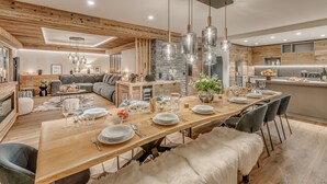 A modern dining area with a long wooden table set for a meal, surrounded by sofas and a stone accent wall. - Spacious apartment, lake view - 14 guests (Tignes)