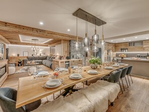 Ein moderner Essbereich mit einem langen Holztisch, der für eine Mahlzeit gedeckt ist, umgeben von Sofas und einer Wand mit Steinverkleidung.