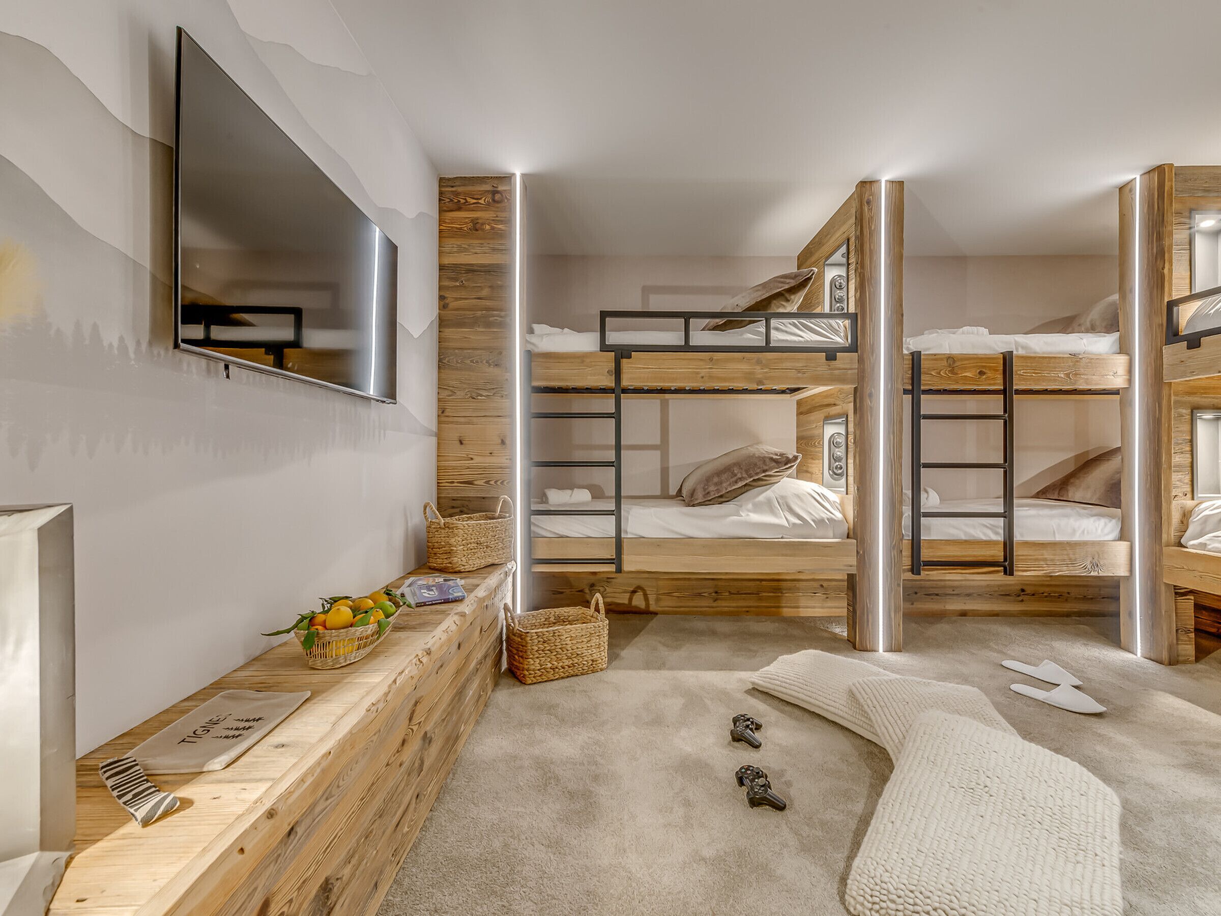 Une chambre moderne avec des lits superposés, un banc en bois, un miroir et une petite table sur laquelle se trouvent des fruits et des clés.