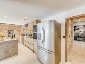 Eine moderne Küche mit Edelstahlkühlschrank, Holzschränken und einer zentralen Kochinsel mit Obst und einer Flasche.