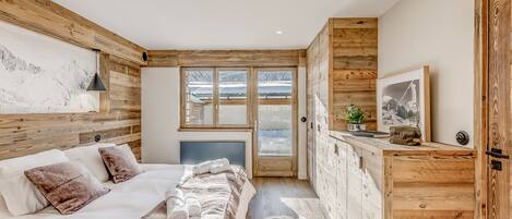 Un dormitorio con cama, paredes de madera, ventana y puerta.