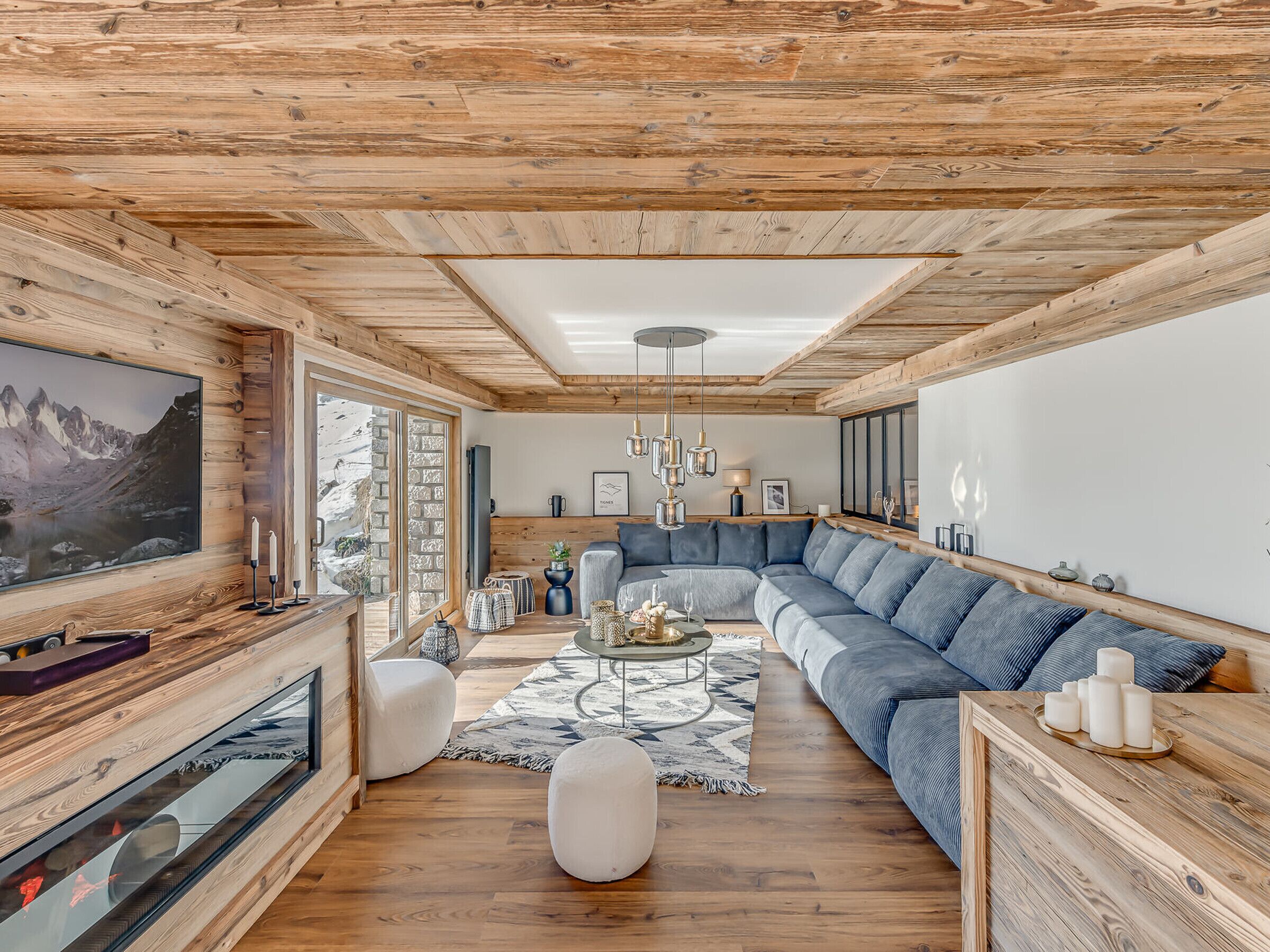 A modern living room with a wooden ceiling, a large TV, a sofa, and a fireplace.