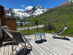 En terrasse med to liggestole og et lille bord, med udsigt over et bjergrigt landskab med en sø og en vej.
