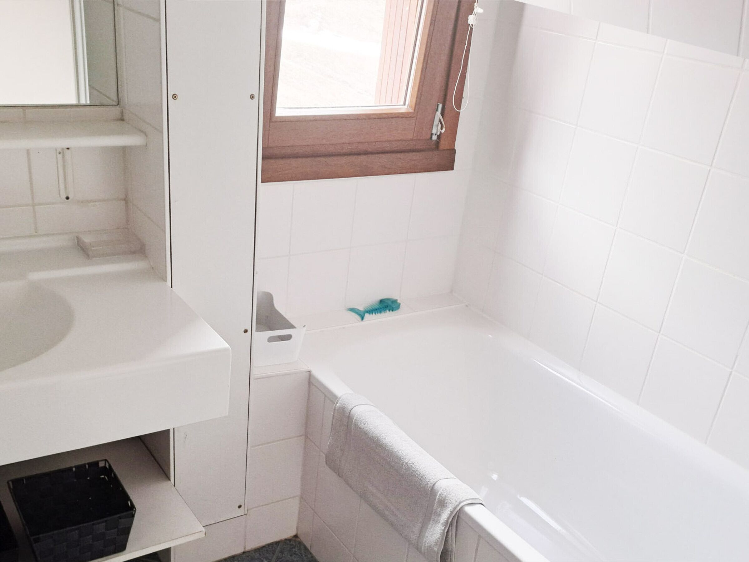 A small bathroom with a white sink, a bathtub, and a window with a wooden frame.