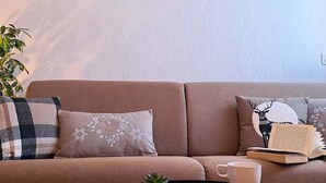 A beige sofa with patterned pillows, a small potted plant, a tray with a mug and biscuits, and a book on a side table. - Functional apartment in the heart of Tignes - 4 guests (Tignes)