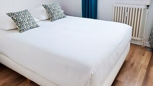 A bed with white bedding and patterned pillows, a radiator, and wooden flooring. - Functional apartment in the heart of Tignes - 4 guests (Tignes)