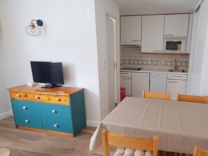 Eine kleine Küche mit weißen Schränken, einer Mikrowelle und einem Spülbecken. Es gibt einen Holztisch mit Stühlen und eine blaue Kommode mit Schubladen.