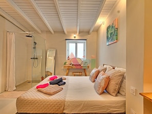 A bedroom with a bed, a bedside table, a mirror, a window, and a shower area. - House with panoramic sea view, pool - 6 guests (Saint-Martin)