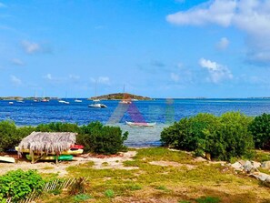 A coastal scene with boats, a thatched-roof hut, and greenery. - House with panoramic sea view, pool - 6 guests (Saint-Martin)