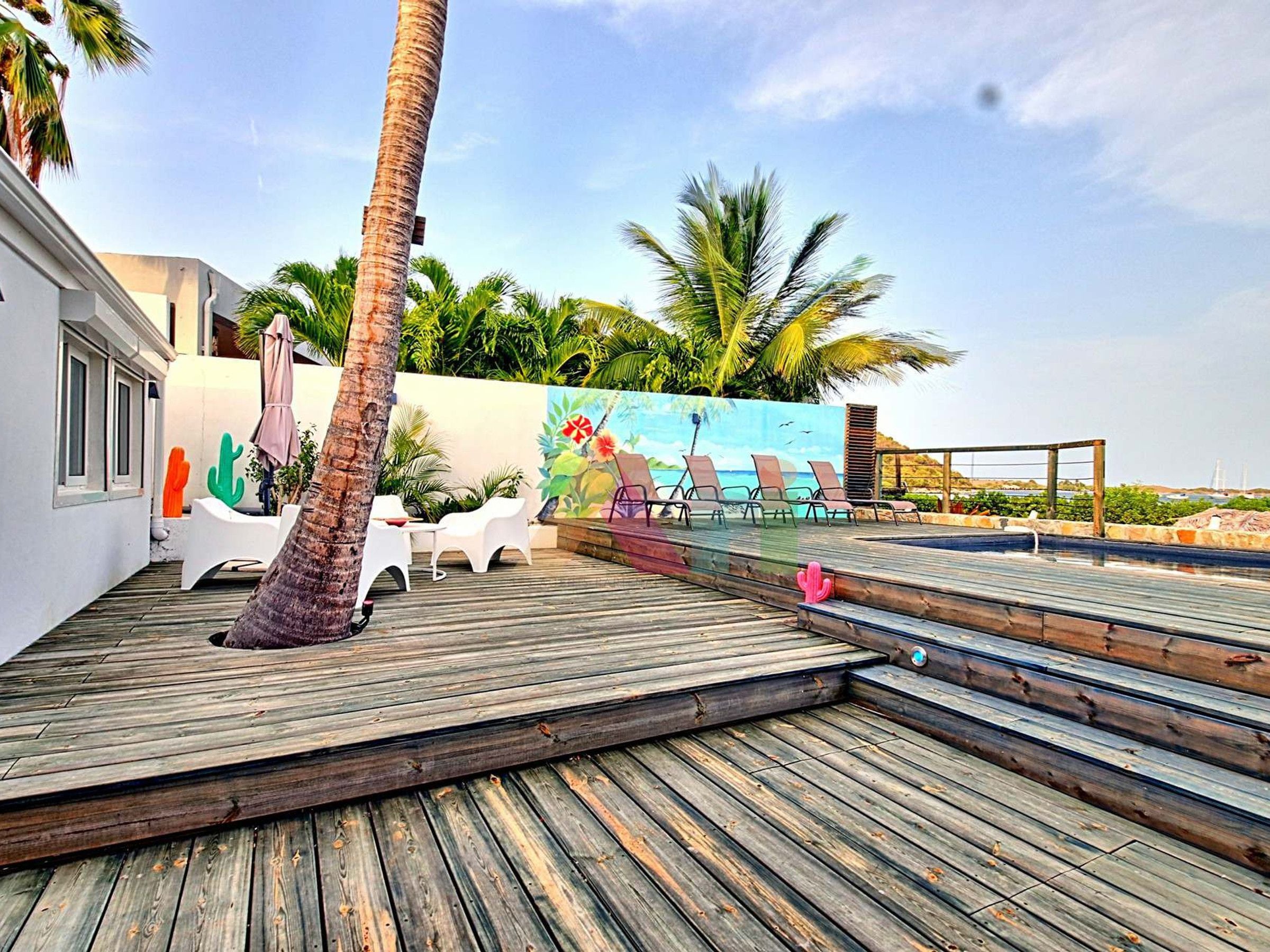 A wooden deck with lounge chairs, a palm tree, and a mural of a beach scene.