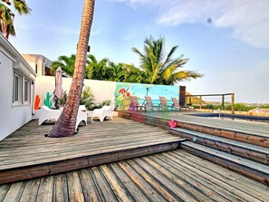 A wooden deck with lounge chairs, a palm tree, and a mural of a beach scene. - House with panoramic sea view, pool - 6 guests (Saint-Martin)