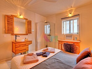 A hotel room with a bed, a wooden vanity with a mirror, a shower, and a window. - House with panoramic sea view, pool - 6 guests (Saint-Martin)