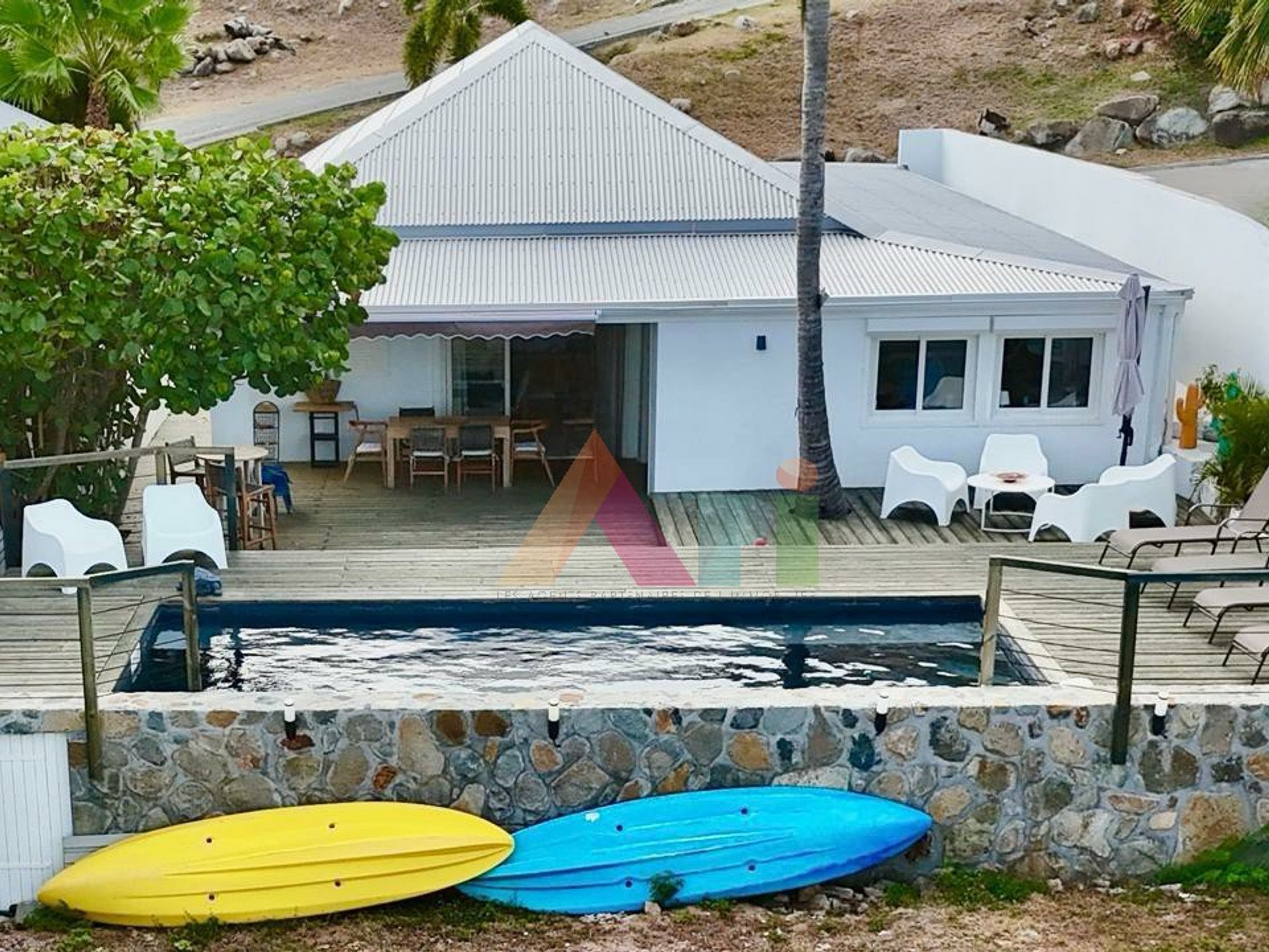 Una casa frente al mar con piscina, mobiliario exterior y kayaks.