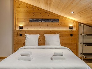 Ein Schlafzimmer mit Holzvertäfelung, einem Bett, zwei Kissen, zwei Wandleuchten, einem gerahmten Bild und einem Metallregal.