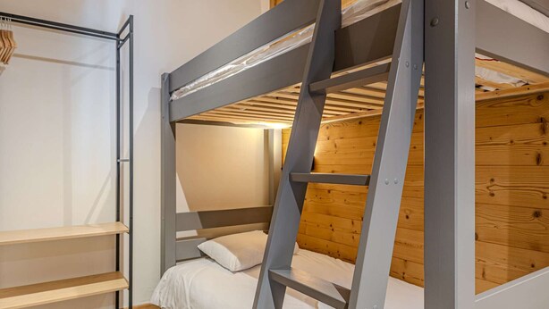 Ein Stockbett mit einer Leiter, einem hölzernen Regal und einer weißen Bettdecke.