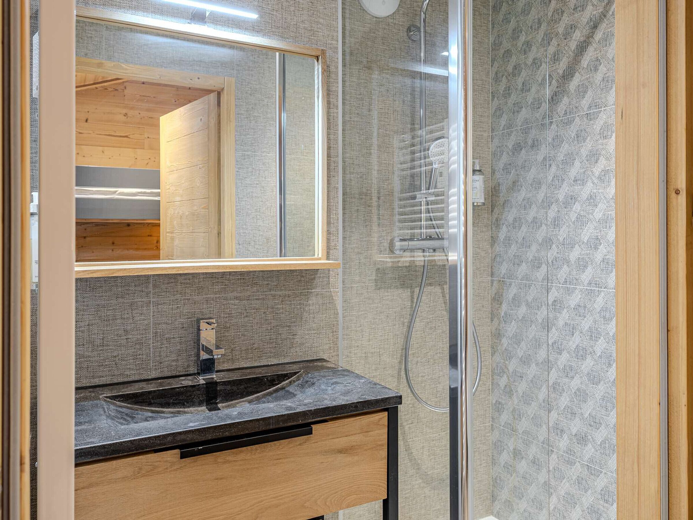 A bathroom with a wooden vanity, a sink, a mirror, and a shower enclosure.