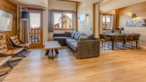 Ein modernes Wohnzimmer mit einer Couch, Sesseln, einem Esstisch und einem Fernseher.