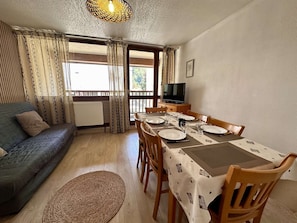 A cozy living room with a sofa, dining table set for four, and a TV on a wooden cabinet. - Central apartment, pets welcome - 6 guests (Saint-Lary-Soulan)