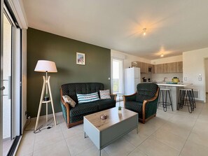 Ein Wohnzimmer mit einer Couch, einem Couchtisch und einer Lampe. Im Hintergrund ist eine Küchenzeile zu sehen.