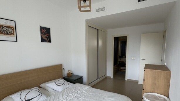 Une chambre à coucher comprenant un lit, une table de chevet, une armoire et une porte donnant sur une autre pièce.