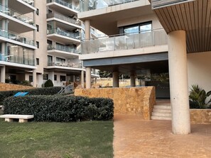 A multi-story building with balconies, a covered entrance, and a landscaped area with a bench and hedges. - Mediterranean comfort apartment - 4 guests (Villajoyosa)