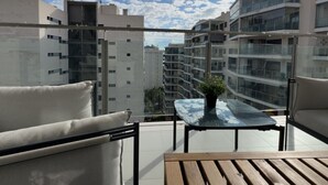 Un balcon donnant sur les bâtiments voisins, une table en verre et un canapé.