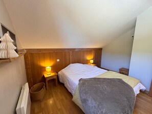 Une chambre à coucher avec une tête de lit en bois, deux tables de chevet avec des lampes, un lit recouvert d’une couverture grise et un radiateur.