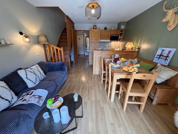 Un salon chaleureux avec un canapé, une table basse et un coin repas comprenant des chaises en bois et une table mise pour le repas.