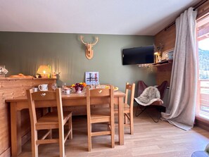 A dining area with a wooden table and chairs, a mounted deer skull on the wall, a television, and a window with curtains. - Apartment mountain view, pets welcome - 6 guests (Vars)