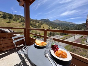 Un balcon avec une table dressée pour deux personnes, offrant une vue sur un paysage montagneux.