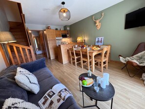 Ein gemütliches Wohnzimmer mit Sofa, einem Esstisch mit Stühlen, einer Küchenzeile und einer Treppe.