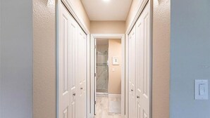 A narrow hallway with white doors, a light-colored floor, and a light switch on the wall. - Walk to Siesta Key Beach and Village - Beautifully Renovated 2BR Condo (Siesta Key)