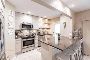 A modern kitchen with stainless steel appliances, a central island with bar stools, and a decorative pineapple on the wall. - Walk to Siesta Key Beach and Village - Beautifully Renovated 2BR Condo (Siesta Key)
