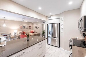 A modern kitchen with a central island, stainless steel appliances, and a dining area with a sofa. - Walk to Siesta Key Beach and Village - Beautifully Renovated 2BR Condo (Siesta Key)