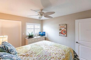 Ein Schlafzimmer mit einem Bett, einem Deckenventilator, einem Fernseher und einer Wanddekoration.
